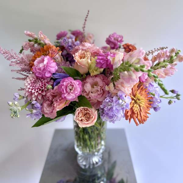 Mixed pink, peach, purple, and orange flowers in a clear glass vase