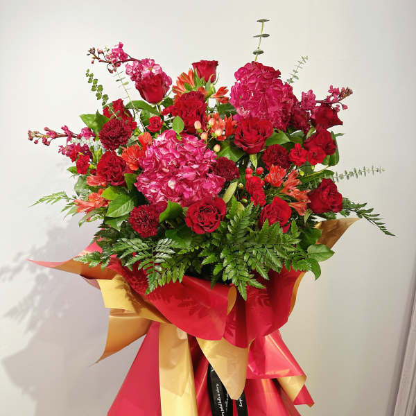 Large bouquet of red and pink flowers wrapped in red and gold paper