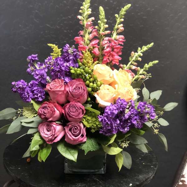 Bouquet of pink and peach roses with purple flowers in a glass vase