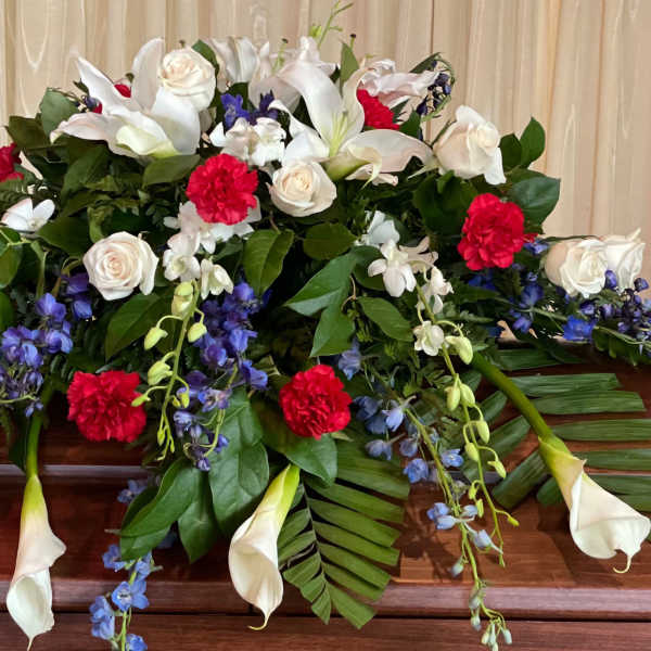 Casket spray with white lilies, roses, red carnations, and blue flowers