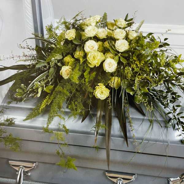 White rose casket spray with cascading greenery on a silver casket