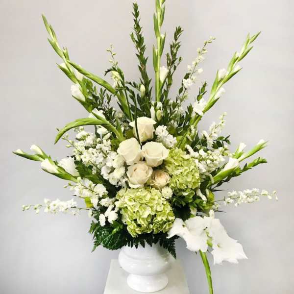 Tall white and green arrangement with roses, hydrangeas and gladiolus in a white pedestal vase