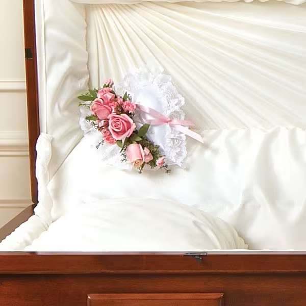 Pink rose corsage with white lace ribbon on a white satin pillow