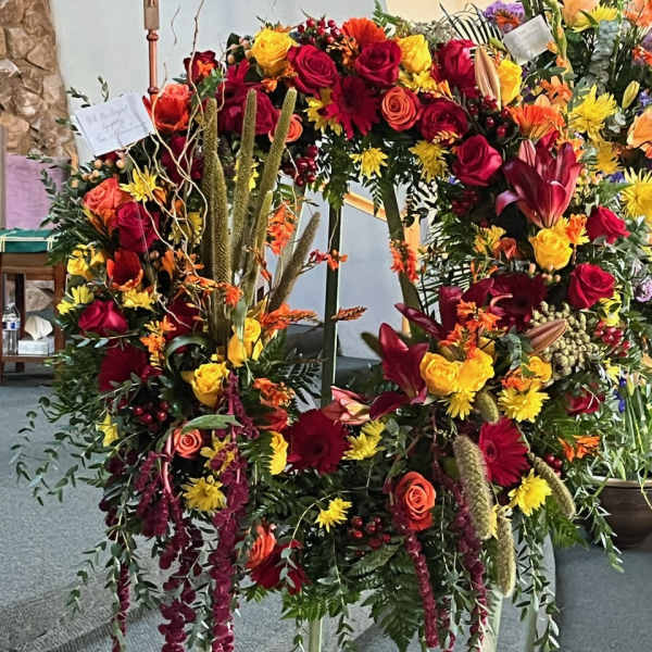 Large standing floral wreath with red, yellow, and orange blooms