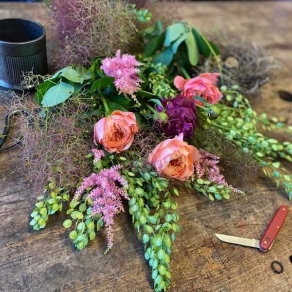 Loose floral arrangement with pink roses and purple blooms on a wooden table
