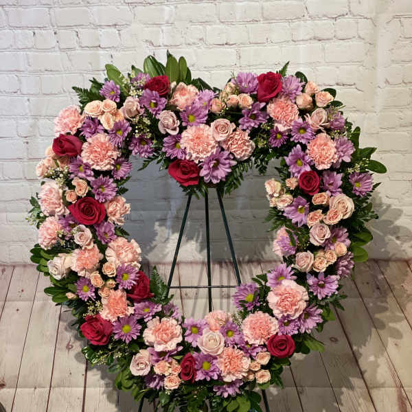 Heart-shaped floral wreath on a stand with pink, purple, and red blooms