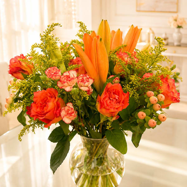 Orange lilies and roses in a clear glass vase