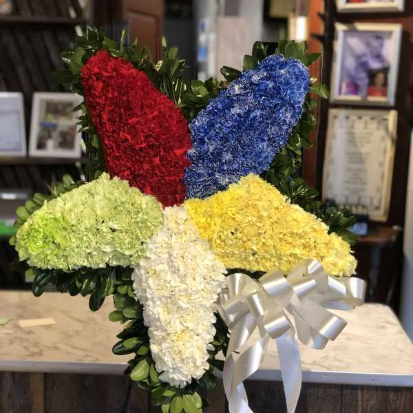 Cross-shaped floral tribute with red, blue, yellow, green, and white flowers