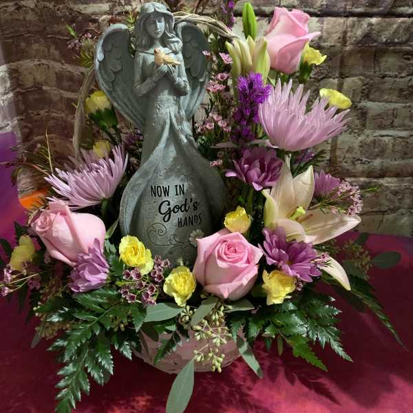 Sympathy flower arrangement with an angel statue and pink and purple blooms