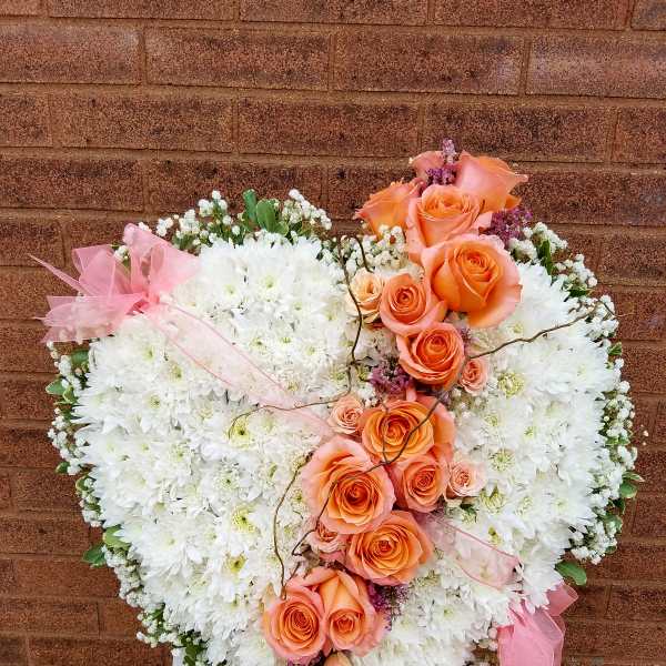 Heart-shaped floral spray with white chrysanthemums and peach roses on a stand