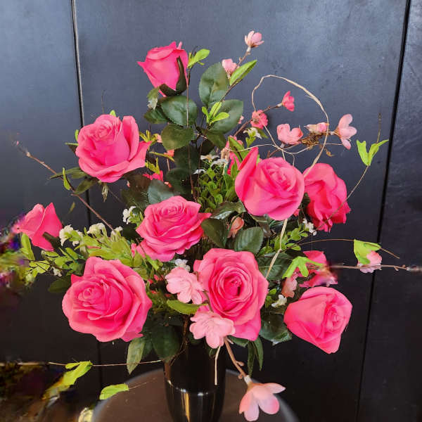 Pink roses arranged in a black vase with small pink blossoms