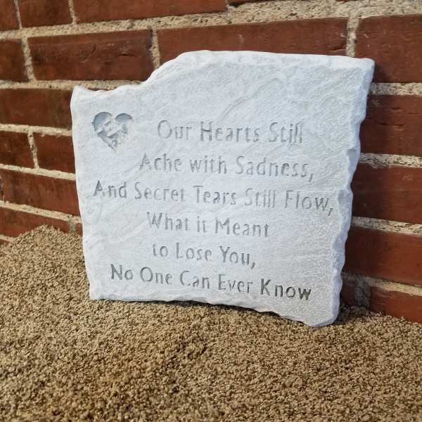 White memorial plaque with an engraved sympathy poem leaning against a brick wall