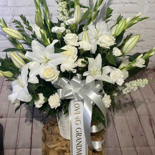 White lilies and roses arranged in a tall bouquet with a silver ribbon