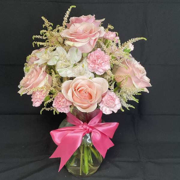 Pink roses and carnations in a glass vase with a bright pink bow