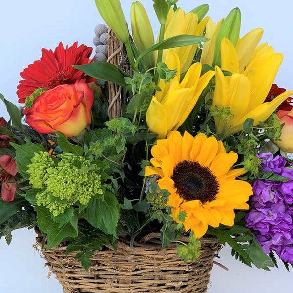 Mixed bouquet in a wicker basket with lilies, roses, sunflowers, and purple blooms