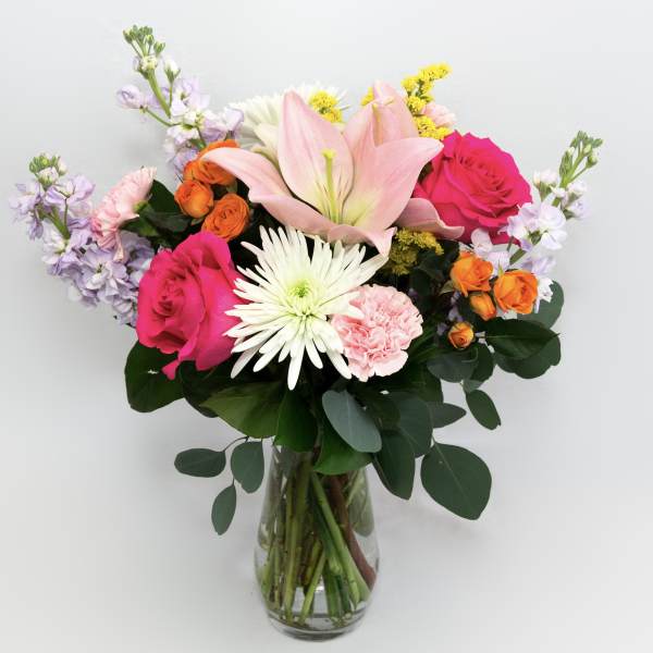 Mixed bouquet of pink, white, orange, and lavender flowers in a glass vase