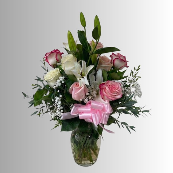 Pink and white rose bouquet with lilies in a glass vase and pink ribbon