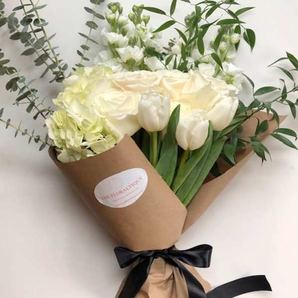 Bouquet of white tulips, roses, and hydrangeas wrapped in brown paper