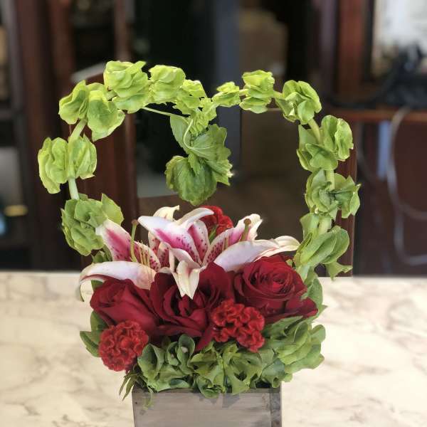 Red roses and pink lilies in a gray square vase with a green floral arch