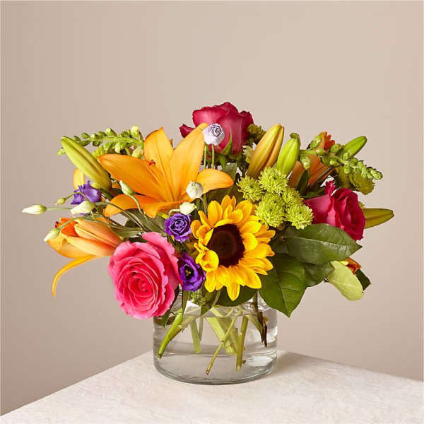 Mixed bouquet of roses, lilies, and a sunflower in a glass vase