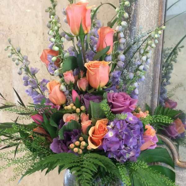 Tall bouquet of peach roses and purple hydrangeas in a glass vase