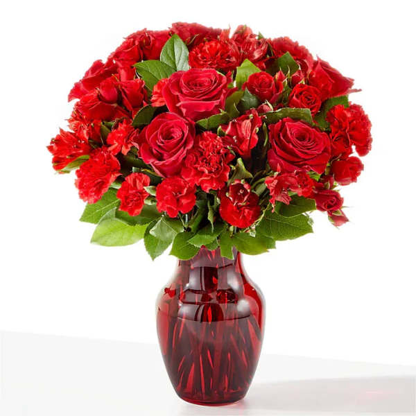 Red roses and carnations arranged in a red glass vase