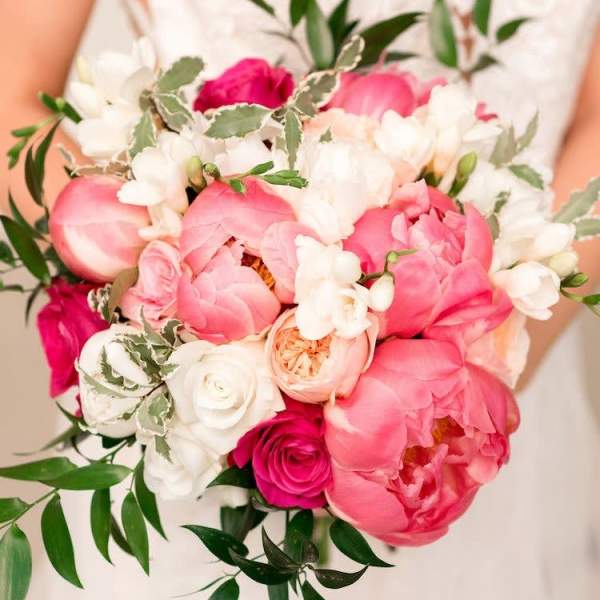Handheld bouquet of pink and white flowers with trailing greenery