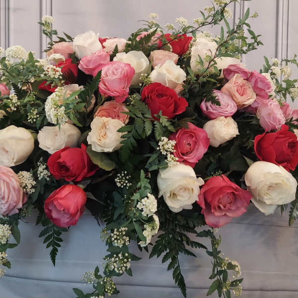 Large arrangement of pink, red, and white roses with trailing greenery
