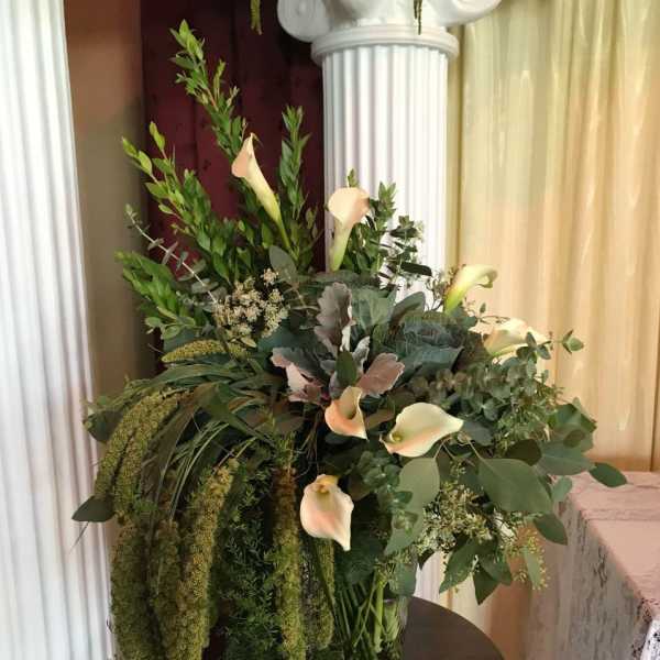 Tall arrangement of cream calla lilies and abundant cascading greenery in a clear glass vase