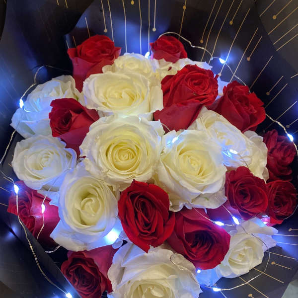 Bouquet of red and white roses wrapped in black paper with string lights