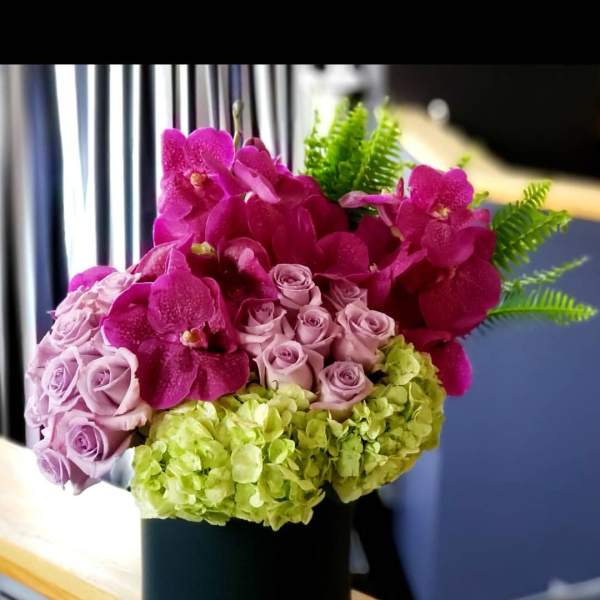 Pink orchids, lavender roses, and green hydrangeas in a black vase