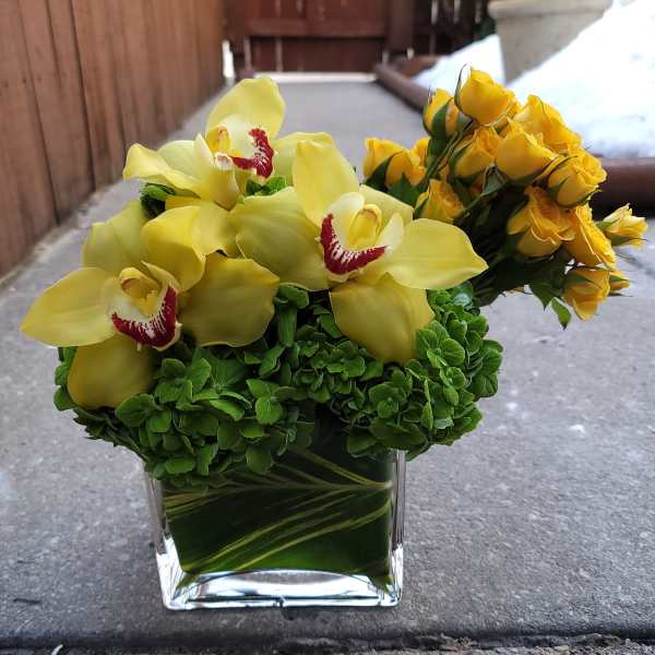Yellow orchids and roses in a clear square vase