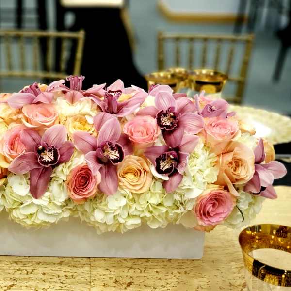 Pink orchids and roses arranged in a white rectangular vase