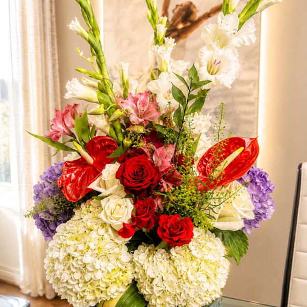 Tall mixed flower arrangement with red roses, white blooms, and purple hydrangeas in a glass vase