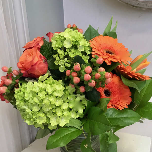 Bouquet of orange roses, green hydrangeas, and orange gerbera daisies in a glass vase