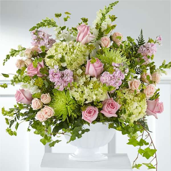 Pink roses and pale green hydrangeas in a white pedestal vase