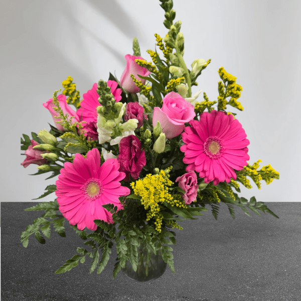 Pink gerberas and roses in a glass vase with yellow filler flowers