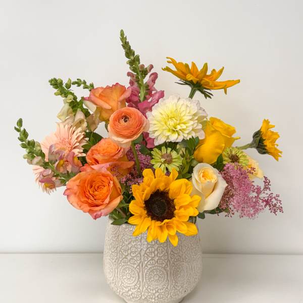 Mixed bouquet of orange, yellow, pink, and white flowers in a patterned vase