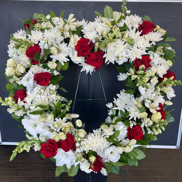 Heart-shaped floral wreath with red roses and white flowers on a stand