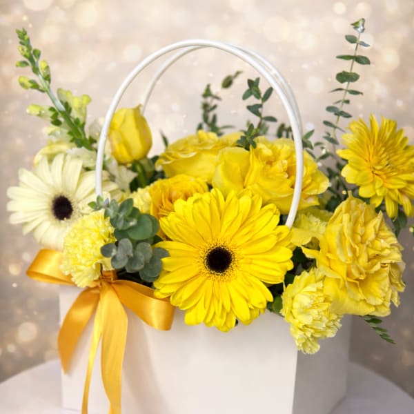 Yellow and white flower arrangement in a white handled box with a yellow ribbon bow.