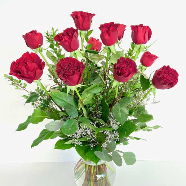 Red roses arranged in a clear glass vase with greenery