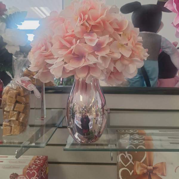 Pink hydrangea bouquet in a reflective vase on a glass shelf