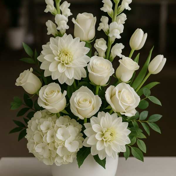 White floral arrangement in a white vase with roses, dahlias, hydrangea, and snapdragons