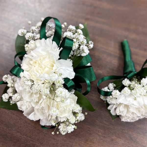 White floral boutonnieres with green ribbon on a wooden surface