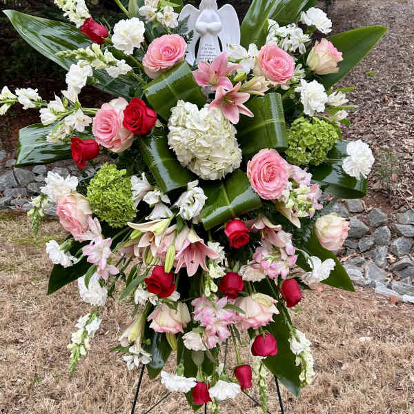 Standing floral spray with pink and red roses, white blooms, and an angel figurine