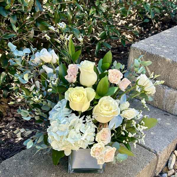 Arrangement of cream roses, pale hydrangea, and eucalyptus in a square glass vase