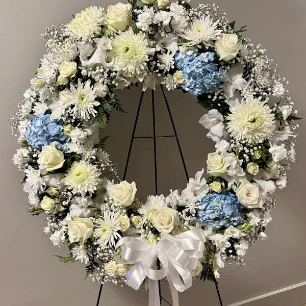 Large white floral wreath with blue hydrangeas on a black stand