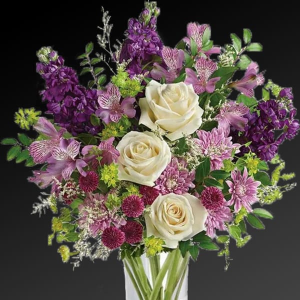 Bouquet of white roses and purple flowers in a clear glass vase