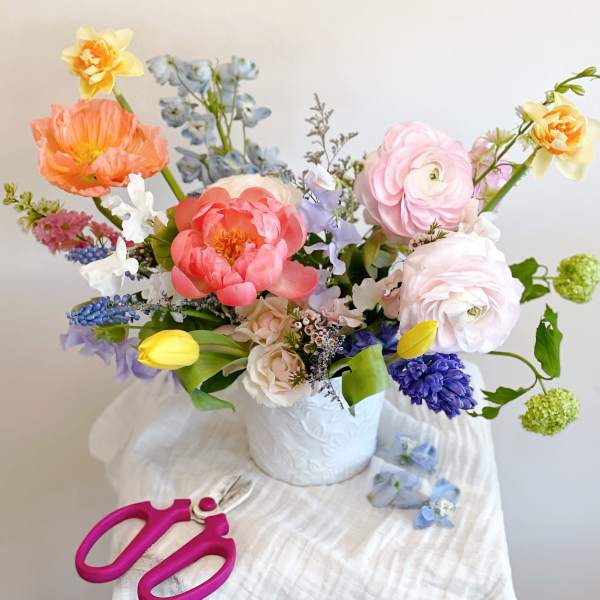 Colorful mixed bouquet in a white vase with pink, peach, yellow, and blue flowers