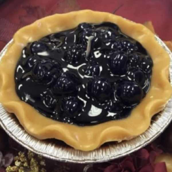 Black candle in a yellow tart-shaped holder on a foil tray